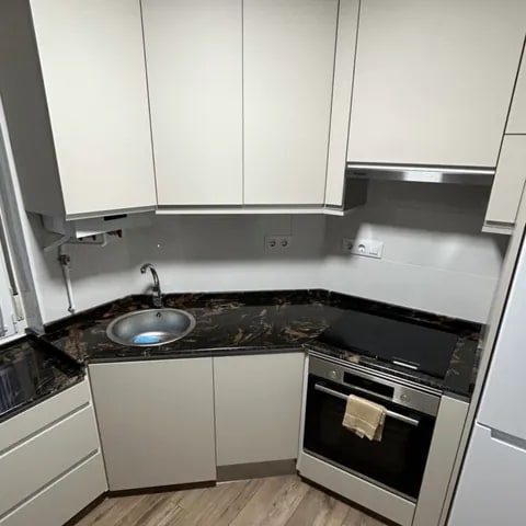 Cocina de carpintería a medida en blanco con encimera oscura - David Carpintería Cocina en esquina con mobiliario de carpintería blanco y encimera oscura veteada